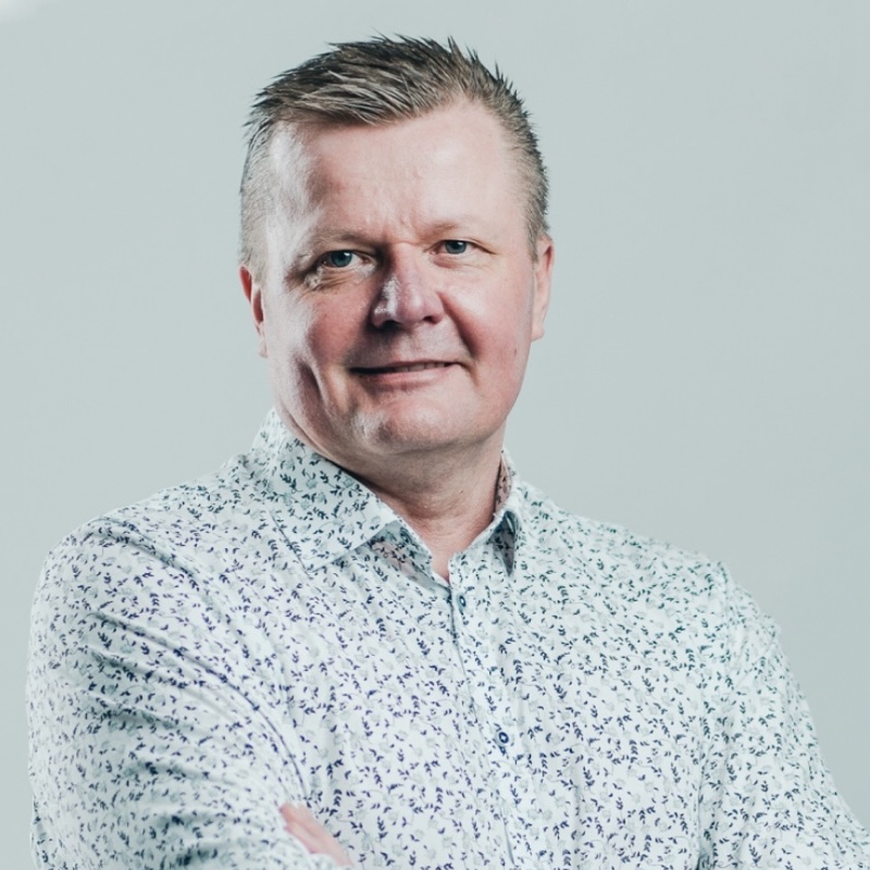 Picture of Mika Punta. Wearing a white dress shirt with small white and blue flowers as pattern. Relaxed style with no tie.