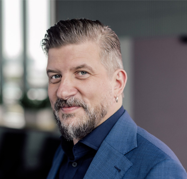 Headshot of Mikael Nylund wearing a blue dress shirt and a blue blazer with no tie.